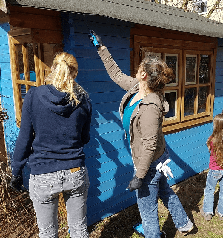 Eltern beim Streichen eines Gartenhauses an einem Grünen Tag